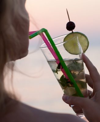 Close-up shot of a woman drinking refreshing mojito cocktail with a straw. Holidays and summer vacation